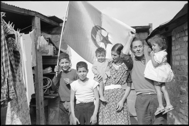 Photo d'une famille joyeuse qui pose devant un drapeau de l'Algérie, dans un bidonville
