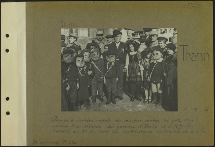Thann. Groupe d'écoliers, munis du masque contre les gaz réunis autour d'un vétéran des guerres d'Italie et de 1870. Les soldats, au deuxième plan, sont les instituteurs militaires de la ville