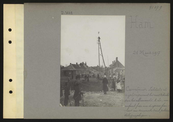 Ham. Carrefour. Soldats et civils réparant les rues détruites par les Allemands. A droite ; un enfant fixe un drapeau français au sommet d'un poteau télégraphique