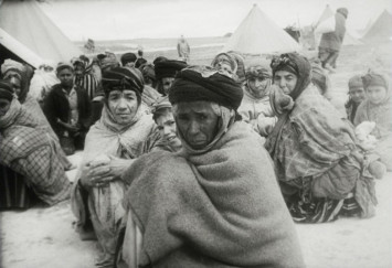 Photo en noir et blanc représentant des réfugiés algériens assis par terre dans un camp de réfugiés