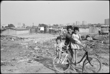 Photo d'une femme et deux enfants sur un vélo, dans un bidonville